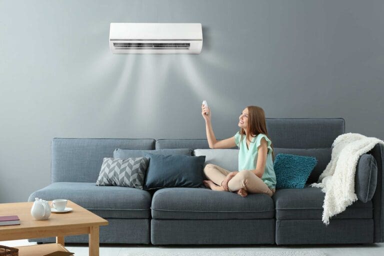 a girl sitting on couch turned on air conditioner with remote control in her hand.