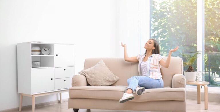 a woman sitting on a couch eyes closed and smiling enjoying fresh indoor environment.