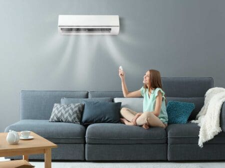 a girl sitting on couch turned on air conditioner with remote control in her hand.