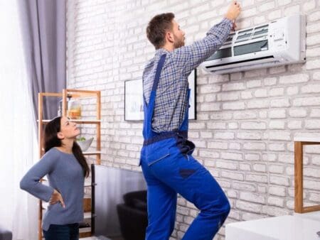 a technician is repairing ac on wall and a girl is standing behind him watching ac repair