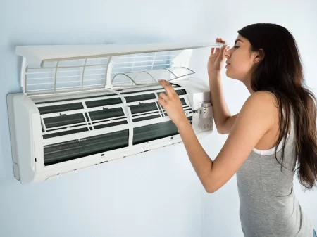 a woman opened indoor unit of air conditioner and looking inside it.